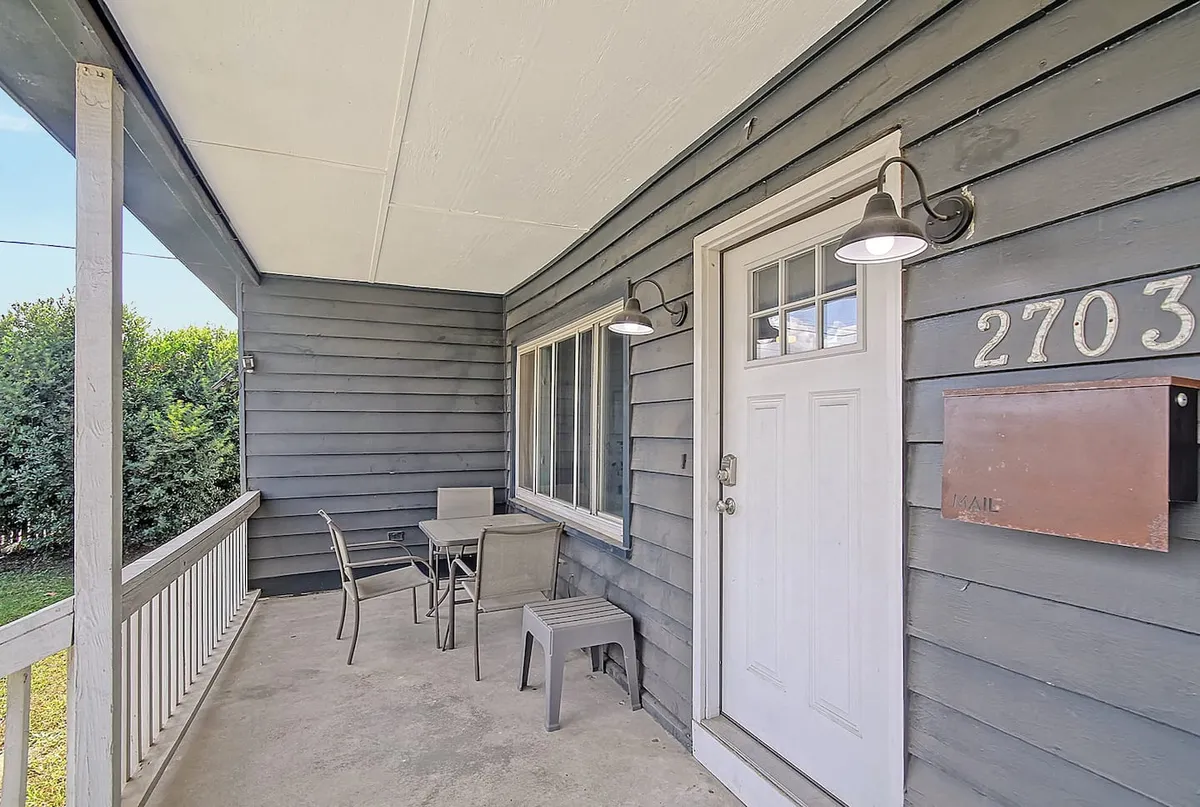 This image captures the front exterior of the house, focusing on the inviting front door, outdoor seating area, and visible house numbers. Warm natural light and cozy outdoor arrangements suggest a welcoming and social atmosphere, perfect for gatherings and group arrivals.