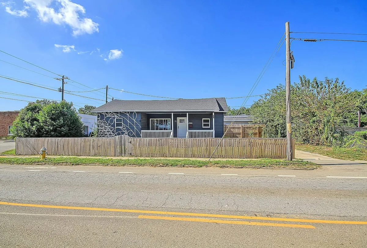 The inviting exterior of the home, featuring a charming front porch with decorative wall design, a fenced yard, and mature landscaping. The porch is set up for relaxation and socializing, evoking a welcoming neighborhood atmosphere.