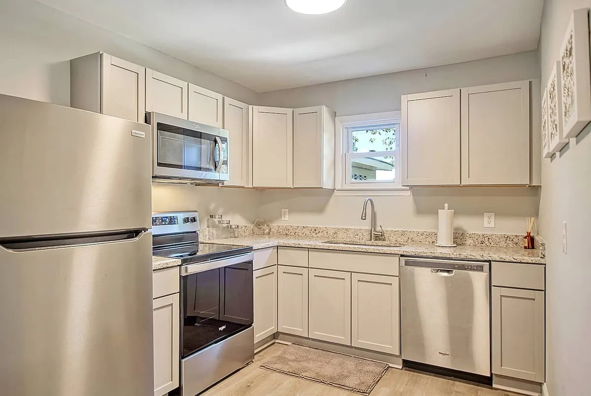 A bright, modern kitchen featuring stainless steel appliances and granite countertops. The window floods the space with natural light, enhancing the welcoming ambiance. The layout is open, making it easy for the chef to interact with others in the adjoining living and dining areas.