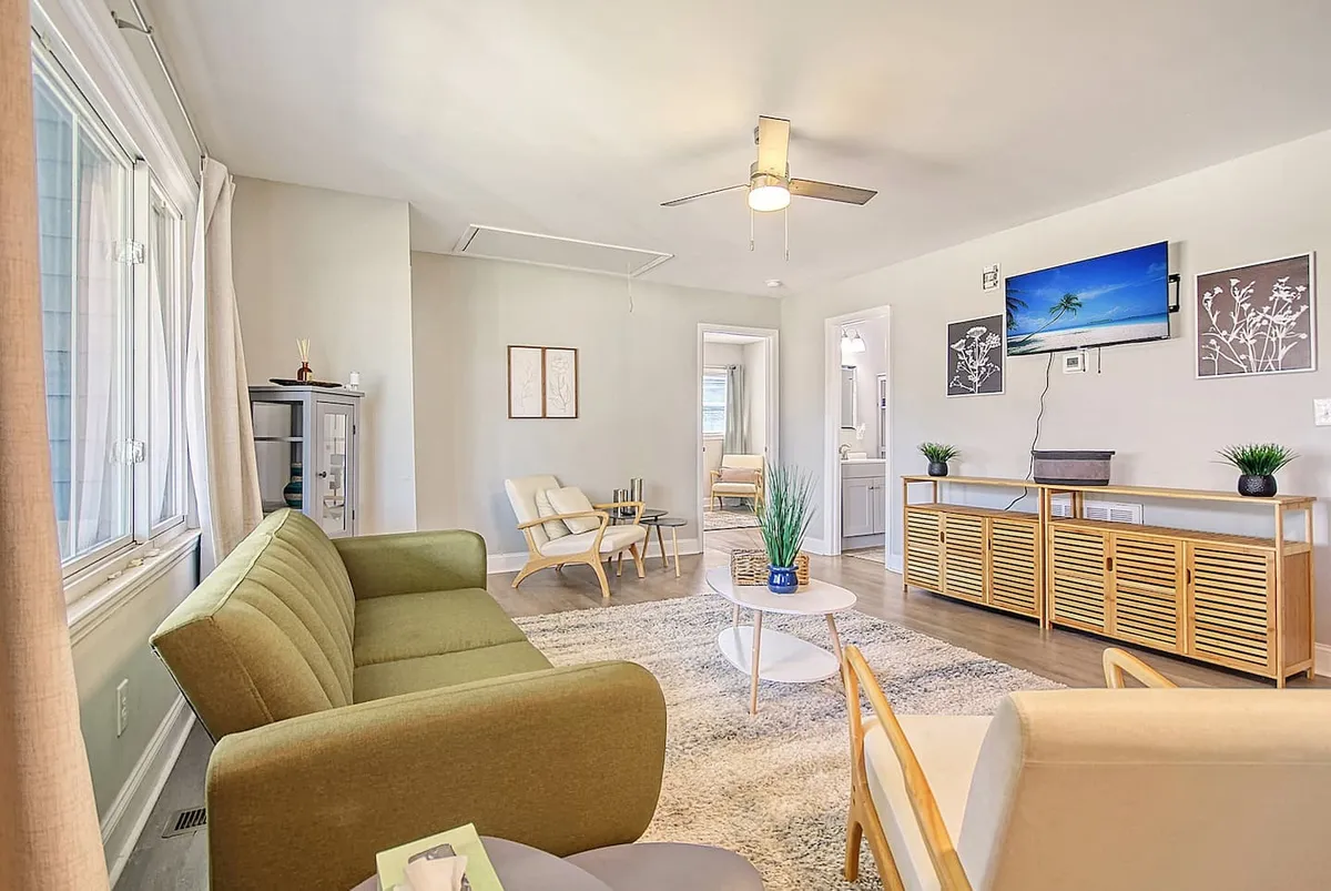 A casual and comfortable living room scene featuring a green sofa, wooden coffee table, wall-mounted TV, and decorative wall art. The setting is tailored to socializing, watching movies, and unwinding, with thoughtful touches that make it feel homey.