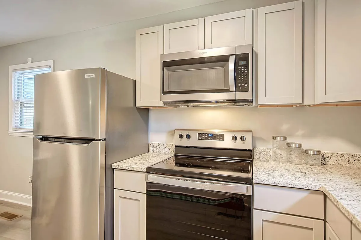 A view of the kitchen highlighting a stainless steel refrigerator, black stove, and expansive granite countertop. The setup is modern and highly functional, inviting meal prep and gatherings. The scene reinforces a sense of togetherness and the kitchen as a hub for activity.