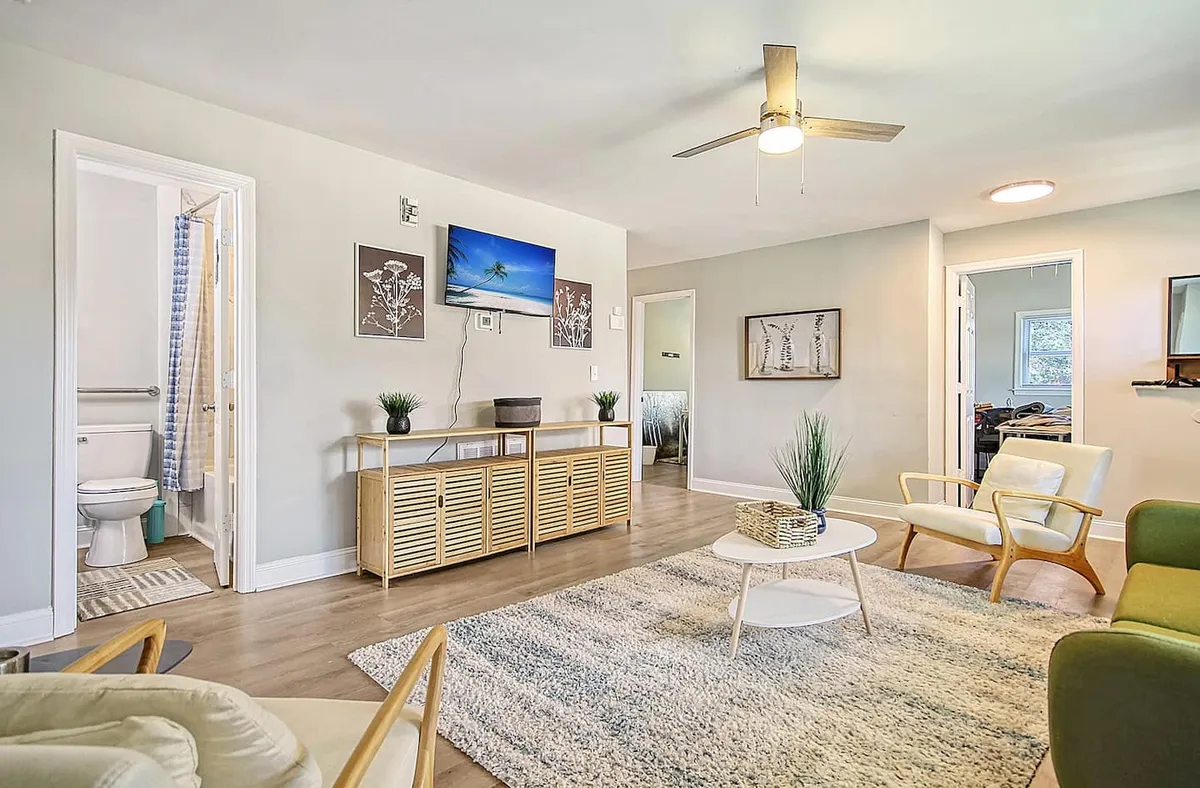 The image showcases a bright and inviting living room with a comfortable sofa, stylish coffee table, tasteful wall art, and a TV, all bathed in natural sunlight. The setting is perfect for relaxing with friends or family, offering a warm atmosphere ideal for downtime between Charleston adventures.