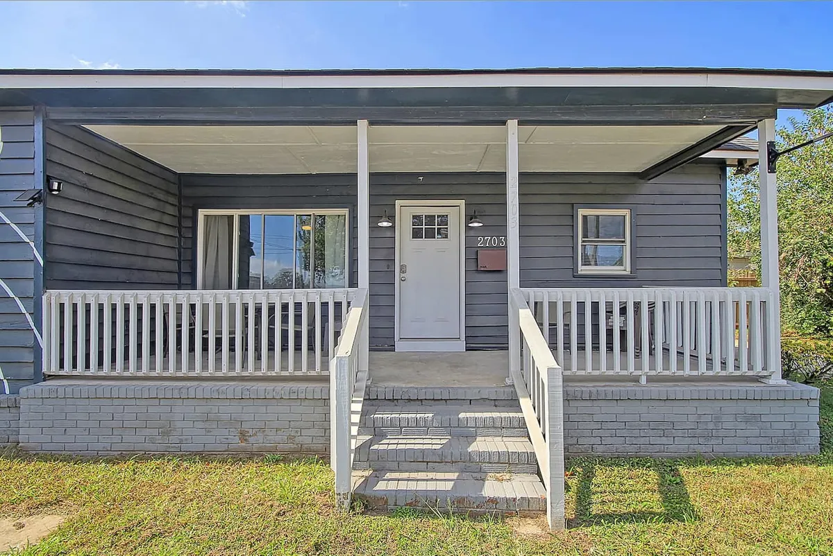 This exterior image showcases the front porch with white railing and the main entrance door, inviting guests into the home. The scene hints at relaxed evenings on the porch or social gatherings, with a welcoming atmosphere that connects the property to its vibrant neighborhood.